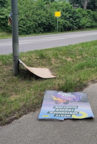 Ein Laternenmast auf einem Grünstreifen neben einer Straße, ein beschädigtes Wahlplakat der Grünen liegt am Boden