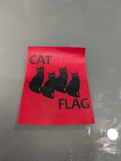 A sticker of a black flag (punk band) logo but with cats on a red background with the words CAT FLAG