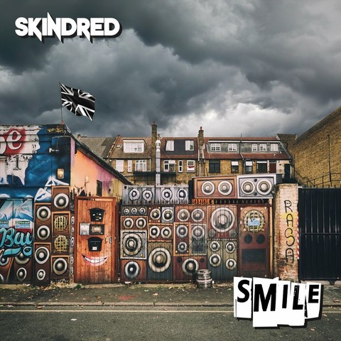 Album cover for Smile by Kindred.

It's a photo of a British street. The fence in the foreground is painted to look like large music amplifiers. A British flag is flying. The sky is overcast.