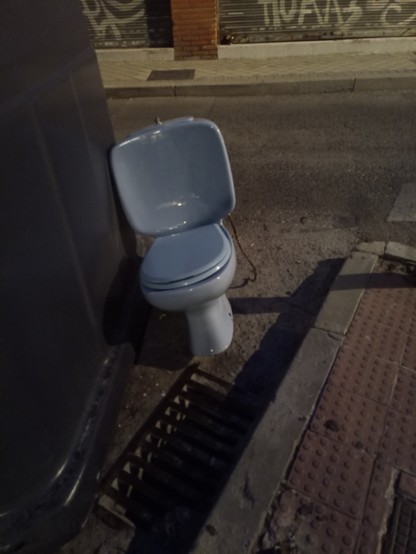 Photo of a blue ceramic toilet leaning against a bin as if it has had too much to drink