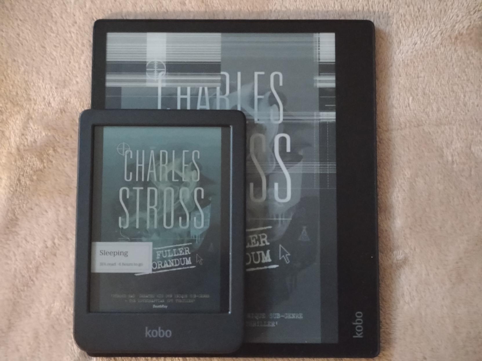 Two kobo devices on top of eachother on a fluffy bed cover. Underneath there's an Elipsa with a broken screen, and on top of it there's a new Clara Coulour. The Clara is much smaller, covering a little less than a third of the Elipsa.

They're both turned off, showing the same book cover for Charlie Stross' "The Fuller Memorandum".
